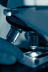 Scientist wearing gloves adjusting glass slide under illuminated microscope lens