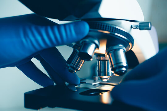 Gloved scientist examining sample slide under laboratory microscope light