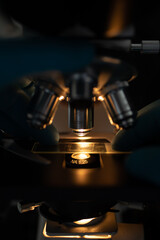 Scientist wearing gloves adjusting glass slide under illuminated microscope lens