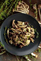 Fried shimeji mushrooms with thyme and garlic on a black plate.