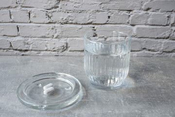 White pill and glass with water stay on the table.