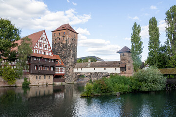 Obraz premium Picturesque view of Henkerhaus Museum, Wasserturm, and the Henkersteg bridges in Nuremberg, Bavaria, spanning the Pegnitz River amid charming medieval architecture.
