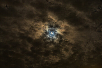 Moon shines through clouds with dramatic blue and gold colored halo 