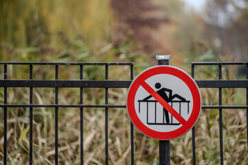 Znak zakazu przechodzenia przez ogrodzenie – czerwony symbol ostrzegawczy na metalowej barierce w parku © Kacper