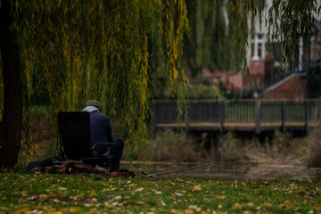Wędkarz nad rzeką w jesiennym parku – spokojna scena z mężczyzną łowiącym ryby pod wierzbą
