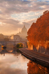 Autumn and foliage in Rome. Beautiful sycamore orange leaves along River Tiber in mist during sunset with iconic St Peter dome