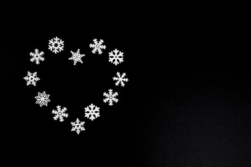 White wooden snowflakes are arranged in a heart shape on a black background. A minimalist winter composition with contrast and copy space.
