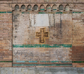 Abstract medieval background made of bricks, terracotta cross, clay decorations, not legible Inscription and ancient enamel. Side of a cubic base for a medieval statue in the center of Bologna