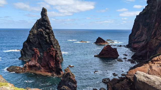 Jagged volcanic sea stacks rising from deep blue ocean along rugged coastal cliffs. Madeira.