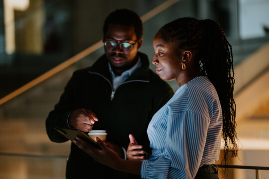 Black business colleagues discussing project on tablet at office night - Powered by Adobe