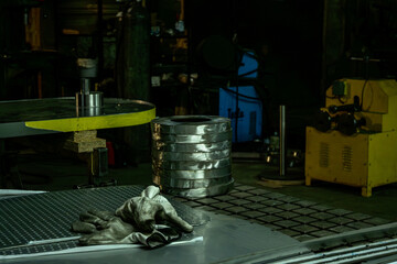 Metal parts and work gloves on a table in an industrial workshop with machinery in the background.