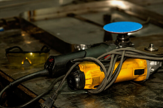 Metal workshop table with grinder, safety glasses and stainless steel parts.