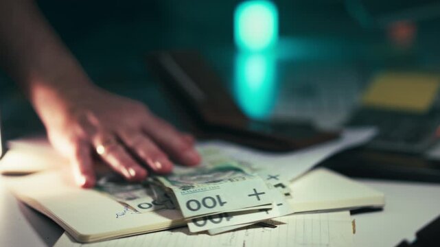 Hand Giving Polish Zloty Banknotes Payment. Close-up male hand placing thick stack 100 PLN bills on desk with notebook documents during financial transaction or salary payout