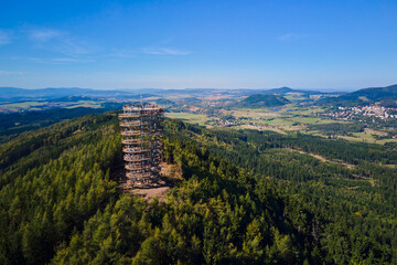 Aerial view of Dzikowiec Wielki observation tower surrounded by green forest and mountains with tourists on top. Concept of sightseeing, outdoor tourism and recreation