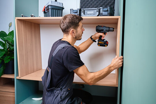 Man drilling hole in side panel of wooden cabinet with electric drill. Home furniture assembly during renovation in apartment