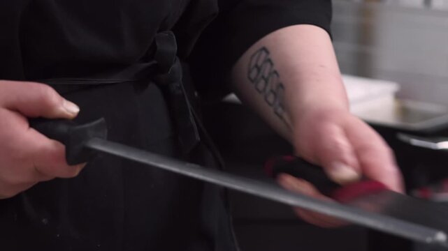 Chef equipment. Preparing kitchen tool. Worker in black uniform using honing steel rod for knife. Professional metal instrument for cooking.