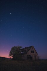 Discover abandoned farmhouse under a vast starry night sky with twilight hues, evoking mystery and solitude.