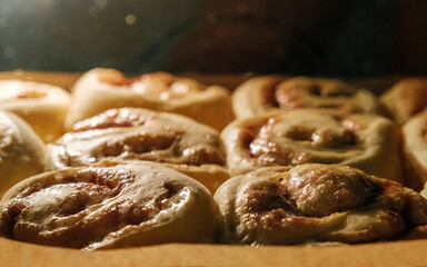Złociste, puszyste bułeczki cynamonowe, proces pieczenia wewnątrz rozgrzanego piekarnika, z naturalnym oświetleniem wpadającym przez szybę.  © PIOTR D