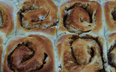 Złociste, puszyste bułeczki cynamonowe z nadzieniem. Bułeczki mają złocistobrązową skórkę i widoczne, wilgotne, karmelizowane nadzienie cynamonowo-cukrowe w spiralnych nacięciach.  © PIOTR D