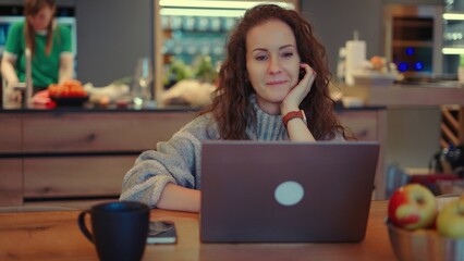 Portrait of middle aged woman sitting at desk. Businesswoman remote working on laptop in home office. Female wearing turtleneck pullover. Happy confident smiling. Autumn or winter indoor clothing.