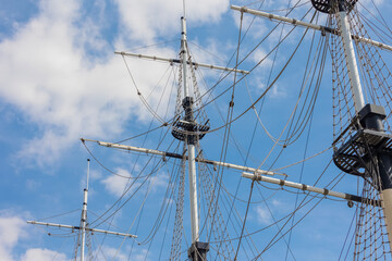 Masts of a sailing ship against a blue sky with clouds.