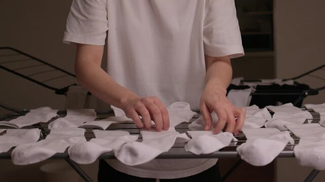 Meticulous pairing and smoothing socks in peaceful routine, Methodically arranging and inspecting white cotton socks on collapsible rack beneath warm illumination