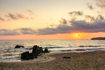sunrise at the sea in summer. landscape with sun and clouds over the horizon. seascape with rock on the sandy beach. vacation season background of bulgaria coast in golden light