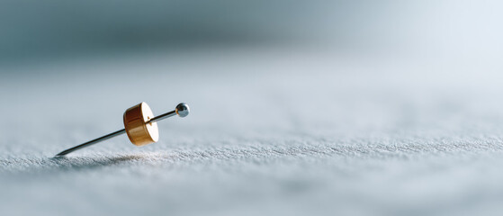 Close-up of a single metallic push pin on textured paper surface with shallow depth of field and soft natural lighting