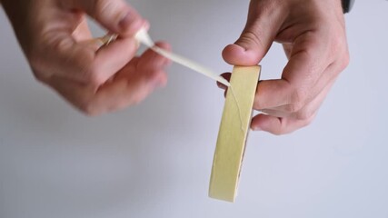 Masking tape in men's hands close-up on a white background top view. He unwinds and tears off a piece of tape. High quality 4K footage. - Powered by Adobe