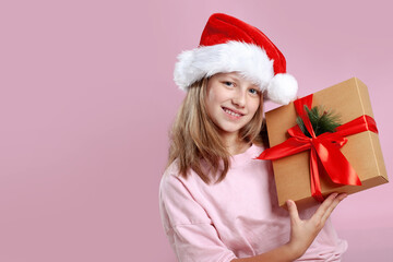 Excited pretty 11-year-old girl in pink T-shirt and Santa hat posing on pink background