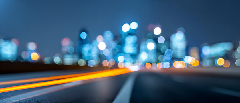 Blurred city skyline at night with glowing bokeh lights and streaks of orange light trails on empty road in foreground