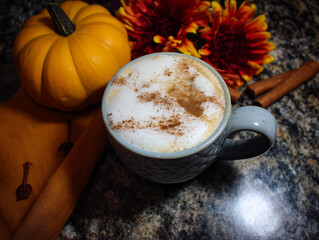 Cozy autumn scene with a pumpkin spice latte topped with cinnamon surrounded by pumpkins and fall flowers.