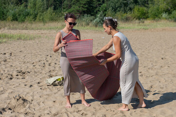Fototapeta premium Two Caucasian women spread a blanket on the beach for a picnic. 