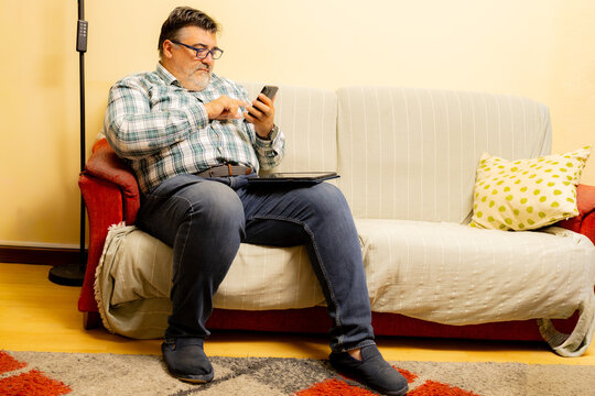 Man relaxing on sofa using smartphone and tablet