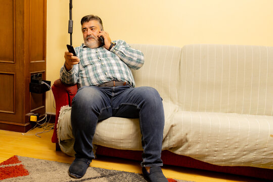 Middle-aged man multitasking, talking on phone and holding remote