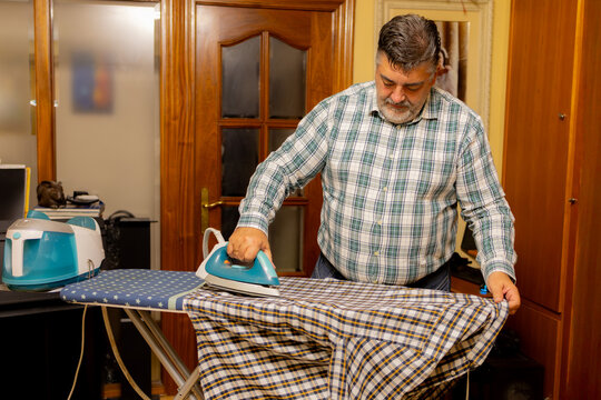 Man ironing plaid shirt at home doing laundry chore