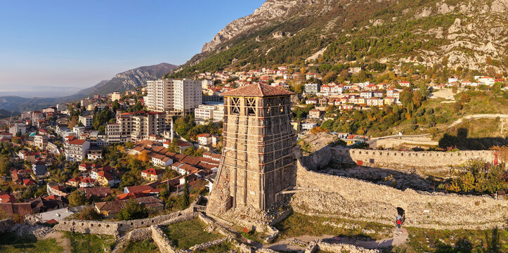 Aerial image of Krujë Castle tower and fortress walls with the city and mountains behind under warm golden afternoon light. - Powered by Adobe