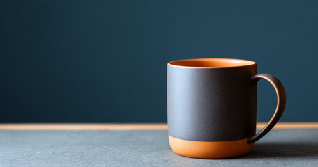 Minimalist ceramic coffee mug with matte black and orange design on gray surface against dark blue background