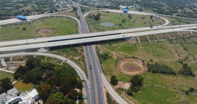 Aerial view of a modern highway interchange in Gujarat, India, showcasing multiple flyovers and well-planned road infrastructure. The cloverleaf junction is surrounded by green fields.