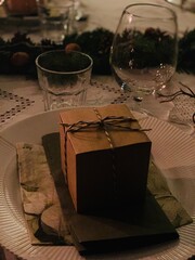 Christmas Table Setting with Gift Box and Holiday Decorations; a small gift box tied with string placed on a plate with festive napkins