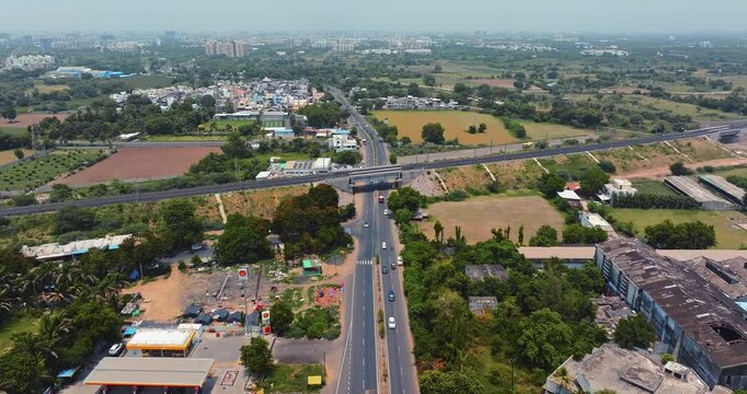 Aerial view of a modern highway interchange in Gujarat, India, showcasing multiple flyovers and well-planned road infrastructure. The cloverleaf junction is surrounded by green fields.