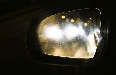 Beschlagener Autoaußenspiegel mit goldbraun-weißen Lichtern vor schwarzem Himmel in der Nacht bei Frost und Kälte im Winter