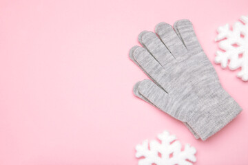 Warm woolen knitted gloves with white snowflakes on pink background
