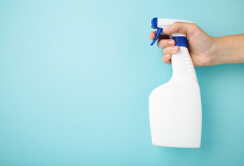 A hand holds a spray of cleaning fluid on blue background.