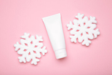 Winter skin care concept. Cosmetic moisturizer cream and snowflakes on pink background.