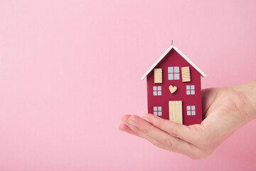 Hands with wooden toy house on pink background. Rent concept