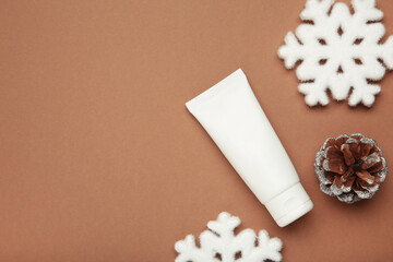 Winter skin care concept. Cosmetic moisturizer cream and snowflakes on brown background.