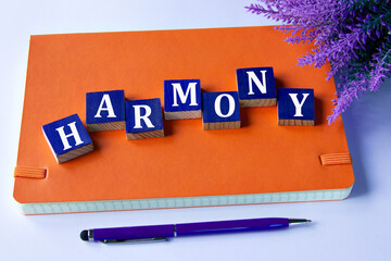 HARMONY - a word written on wooden cubes on an orange notepad with a pen lying nearby