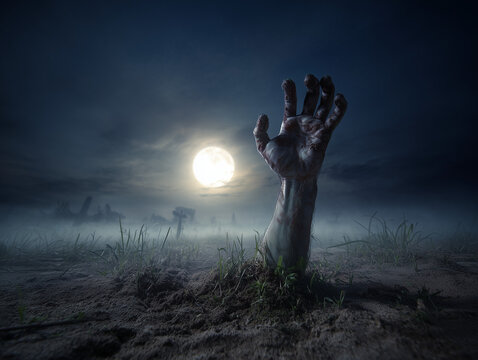 Zombie hand emerging from grave reaching for full moon in cemetery