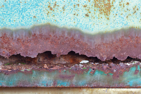 Aged metal surface with peeling blue paint and horizontal rust band.